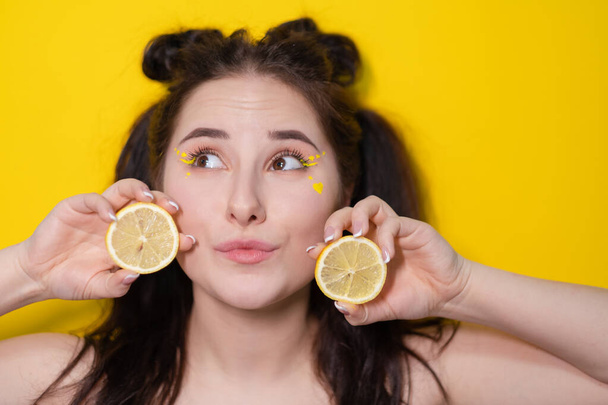 mladá žena s citronovými plátky, brunetka s holými rameny držící citron blízko obličeje na žlutém pozadí. citrusové plody, zdravé jídlo. chutné šťavnaté ovoce. - Fotografie, Obrázek