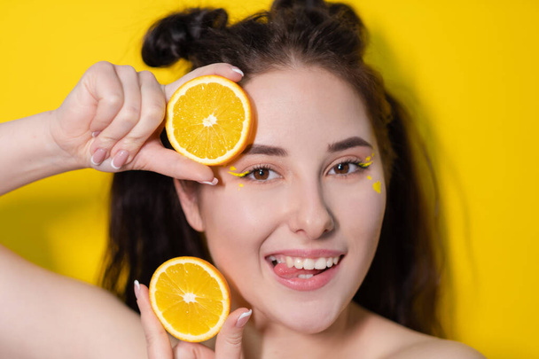 young brunette woman girl with slice of orange fruit near skin face on yellow background. tasty juicy fruit. Tropical fruits, Healthy food. citrus slice. tasty juicy fruit - Φωτογραφία, εικόνα