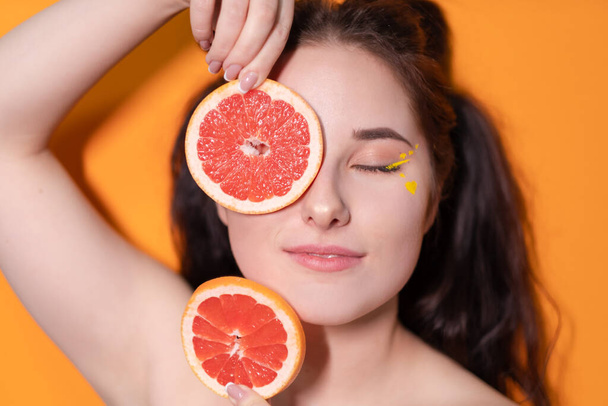 オレンジ色の背景にグレープフルーツのスライスを持つ若い女性 - 写真・画像