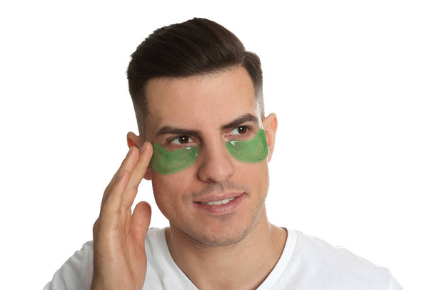 Man applying green under eye patch on white background - Fotoğraf, Görsel
