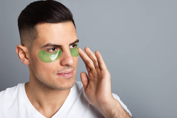 Man applying green under eye patch on grey background. Space for text - Фото, зображення