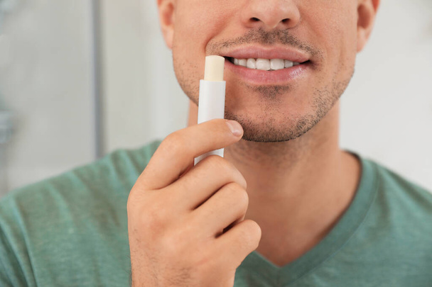 Man applying hygienic lip balm indoors, closeup - 写真・画像