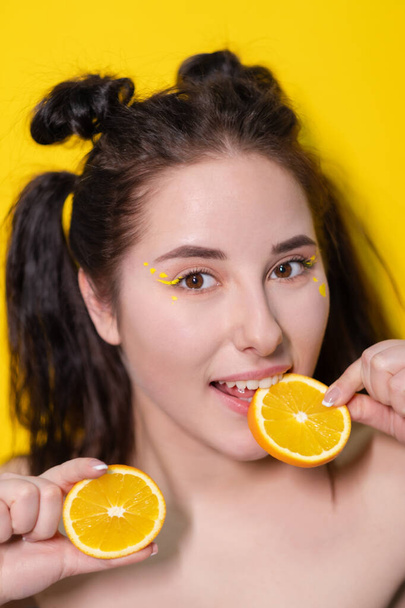 young brunette woman girl with slice of orange fruit near skin face on yellow background. tasty juicy fruit. Tropical fruits, Healthy food. citrus slice. tasty juicy fruit - Photo, Image