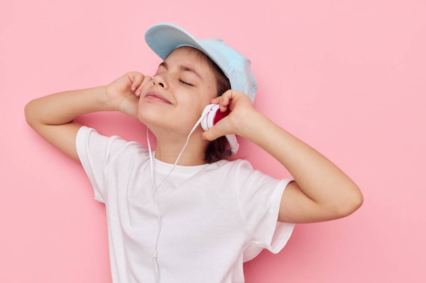 cute girl headphones in a white t-shirt and a cap pink background - Zdjęcie, obraz