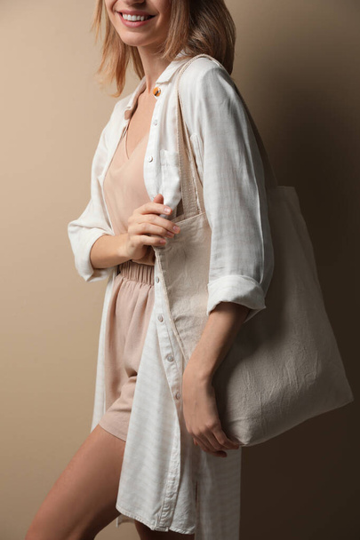 Happy young woman with blank eco friendly bag against beige background, closeup - Φωτογραφία, εικόνα