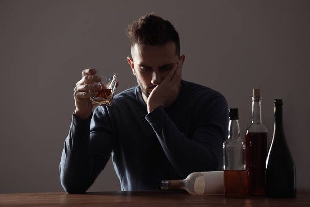 Hombre adicto con bebida alcohólica en la mesa de madera en el interior - Foto, Imagen