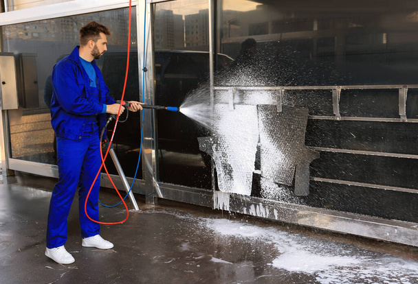 Worker cleaning auto mats with high pressure foam jet at car wash - Foto, Bild