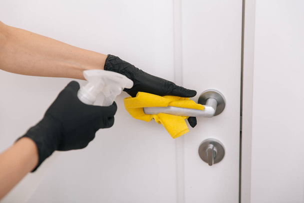 Cleaning door handle with yellow wipe in black gloves and sanitizer spray. Disinfection in hospital and public spaces against corona virus. Woman hand using towel for cleaning - Fotó, kép