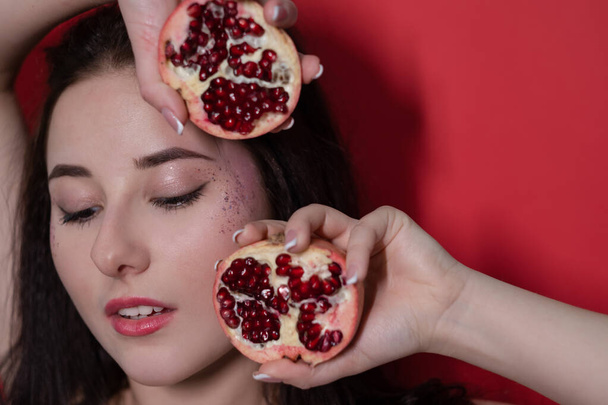 portrait brunette woman girl female with pomegranate near face on red background. tasty juicy fruit - Foto, Imagen