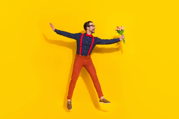 Full size photo of young man jump up give bunch of tulips holiday isolated over yellow color background - Photo, Image