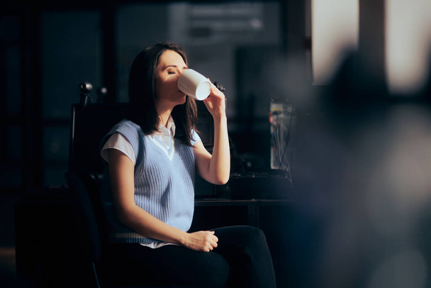 Office Employee Drinking Coffee Sitting at her Desk Arriving First at Work - 写真・画像