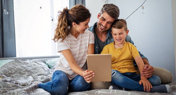 Happy young family spending time at home and looking something fanny on tablet. - Photo, image