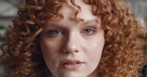 Gros plan portrait d'une jeune femme rousse aux cheveux bouclés regarde la caméra et clignote des yeux, à l'intérieur à la maison - Séquence, vidéo