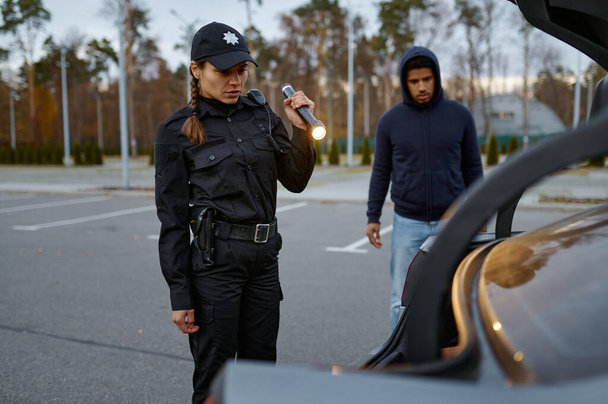 Женщина-полицейский осматривает машину фонариком - Фото, изображение