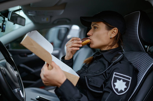 Vrouwelijke politieagent eet donut in auto - Foto, afbeelding