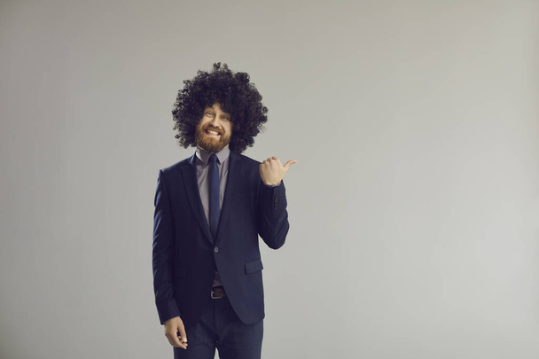 Funny guy in big curly wig pointing thumb away to advertising copy space background - Foto, immagini