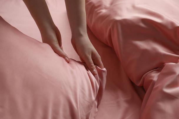 Женщина делает кровать с красивым розовым шелковым постельным бельем, вид крупным планом - Фото, изображение