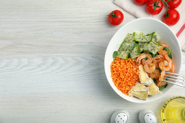 Delicious lentil bowl with shrimps, soft cheese and cucumber on white wooden table, flat lay. Space for text - Foto, Imagen