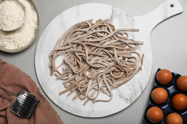 Uncooked homemade soba (buckwheat noodles) and ingredients on grey table, flat lay - Photo, image