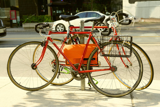 Kaksi punaista lukittu vanha maantiepyörät pudota ohjaustanko ympyrä metalli polkupyörän teline kaupungin kadulla puolella kävellä  - Valokuva, kuva