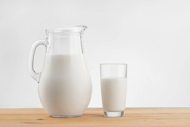 een glazen kan met melk en een glazen standaard op een houten tafel met een linnen tafelkleed - Foto, afbeelding