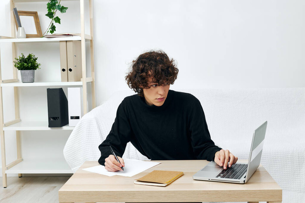 curly guy sitting on the couch at the table in front of a laptop living room - Photo, Image