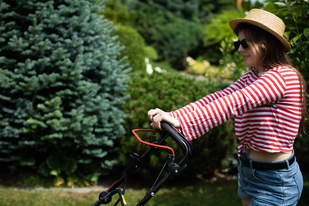 Ένα κορίτσι κρατάει το χερούλι από μια μηχανή του κήπου στα χέρια της.. - Φωτογραφία, εικόνα