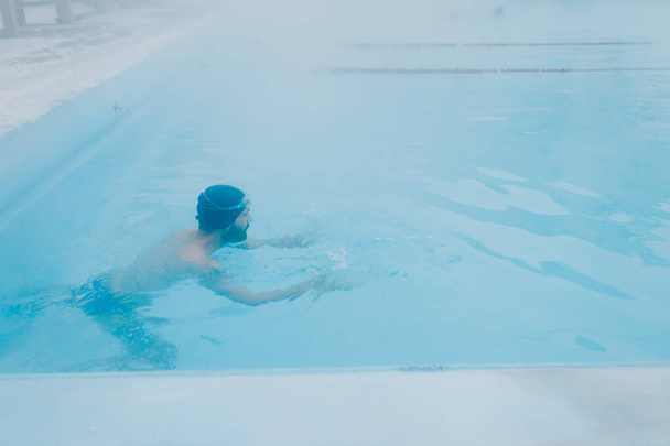 Fit swimmer male training swim in open winter swimming pool with fog. Geothermal outdoor spa concept. - Photo, Image