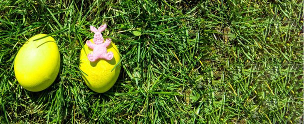 Bir tavşan oyuncağı ve yeşil çimlerde iki dekoratif Paskalya yumurtası. Üst görünüm, boşluk ve metin alanını sağda kopyala. - Fotoğraf, Görsel