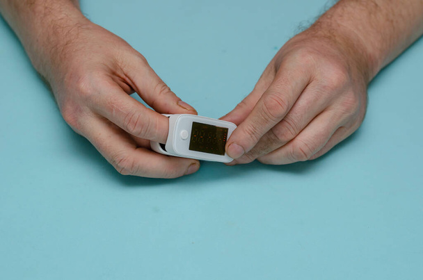 Ein erwachsener Mann hält ein Pulsoximeter an seinem Zeigefinger. Pulseoximeter ist ein medizinisches Überwachungs- und Diagnosegerät zur Messung der Sauerstoffsättigung im Kapillarblut. Selektiver Fokus - Foto, Bild
