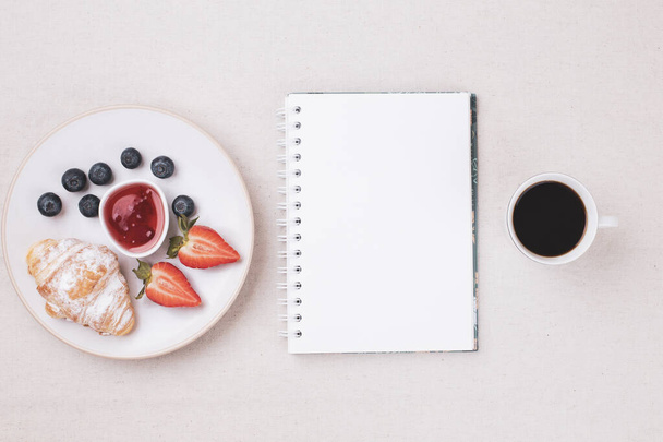 Top view of empty diary and cup of coffee, fresh croissant, jam, ripe blueberries and strawberries on white table, flat lay, copy space - Valokuva, kuva