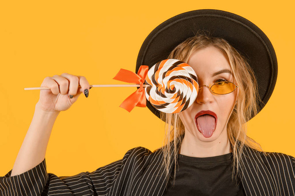 young attractive   white blonde woman in a black hat with a lollipop on a yellow  - Foto, Imagem