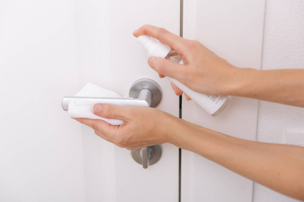 Cleaning black door handles with an antiseptic white wet wipe and sanitizer spray. Sanitize surfaces prevention in hospital and public spaces against corona virus. Woman hand using towel for cleaning - Foto, afbeelding