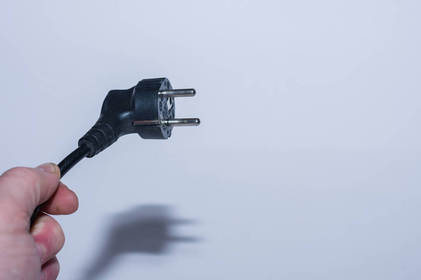 stekker van elektriciteit schuin gehouden in een hand bespaar elektriciteit links zicht met grijze achtergrond - Foto, afbeelding
