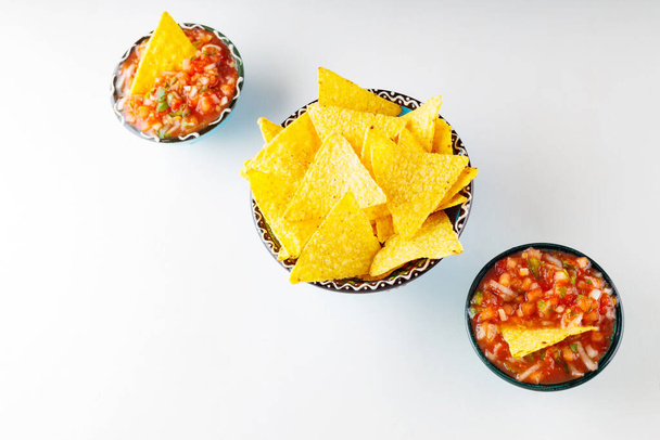 Two bowls with salsa sauce and nacho chips on a white background. Tortilla chips and salsa dip in bowl. Mexican cuisine concept. Top view. Copy space - Fotoğraf, Görsel