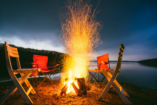 Zapierające dech w piersiach ognisko z krzesłami na tle spektakularnego zalesionego jeziora o zmierzchu. - Zdjęcie, obraz