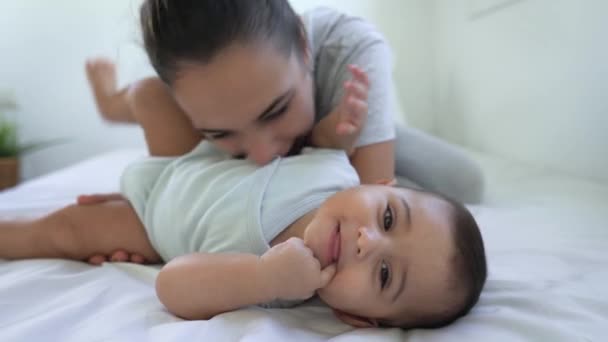 Felice madre giocare con il suo bambino sdraiato insieme sul letto - Filmati, video