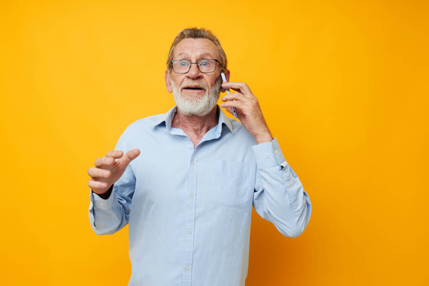 Portrait elderly man gray beard with glasses talking on the phone yellow background - Foto, Imagen