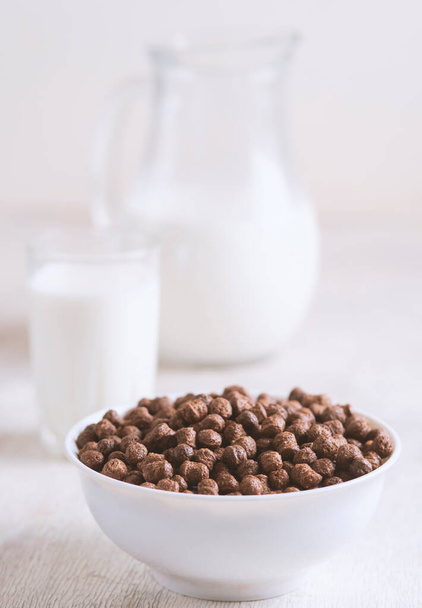 Bowl with chocolate corn balls and milk, on white wooden background. - Фото, изображение