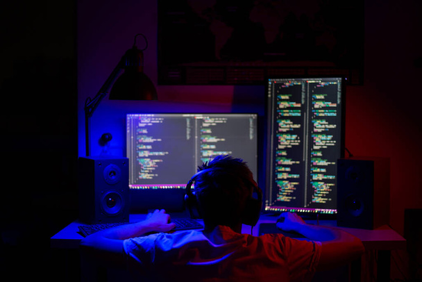 Ребенок сидит за компьютером в комнате за столом ночью с голубым освещением и программами - Фото, изображение