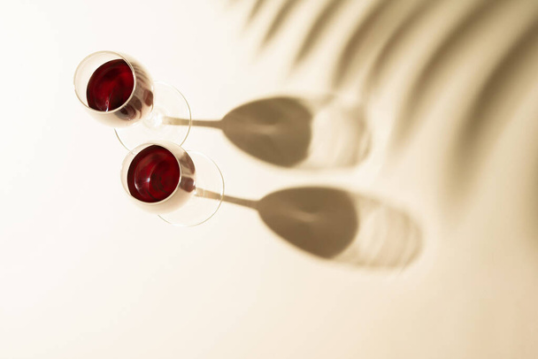 ヤシの葉の影を持つ赤ワインの2つのガラス。バレンタインデーや愛の概念。平敷. - 写真・画像