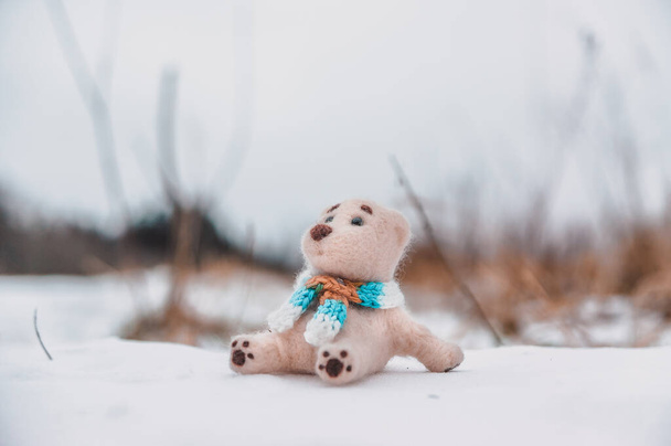 Eşarplı oyuncak bir kutup ayısı karlı kış tarlasında oturur ve baharı bekler. - Fotoğraf, Görsel