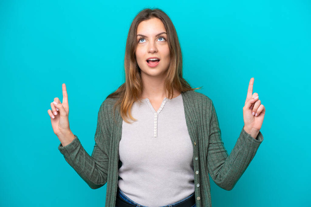 Young caucasian woman isolated on blue background surprised and pointing up - Photo, image