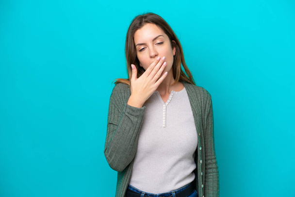 Mujer joven caucásica aislada sobre fondo azul bostezando y cubriendo la boca abierta con la mano - Foto, Imagen