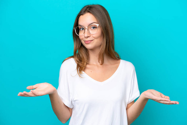 Young caucasian woman isolated on blue background With glasses and having doubts - Photo, Image
