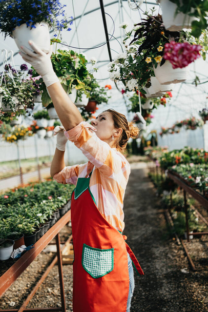 Happy and positive young adult woman working in greenhouse and enjoying in beautiful flowers. - Fotoğraf, Görsel