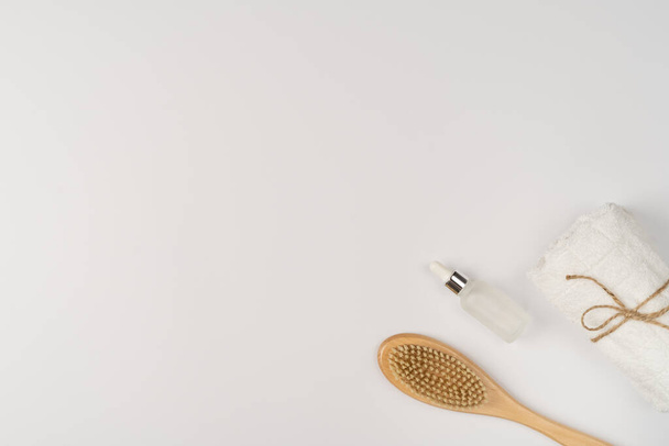 Flat lay, a set of bath products. Eco-friendly wooden brush, clean fresh towel and oil serum for face and body on a white background. - Fotografie, Obrázek