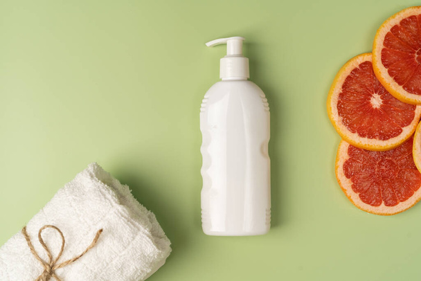 Zitrushaarpflege mit Vitamin C. Weiße Flasche Shampoo oder Lotion, sauberes frisches Handtuch und Grapefruitscheiben auf hellgrünem Hintergrund. - Foto, Bild