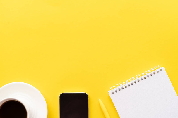 Flat lay, top view office table desk. Workspace with notebook, office supplies, pen,  mobile phone and coffee cup with copy space on yellow background. - 写真・画像