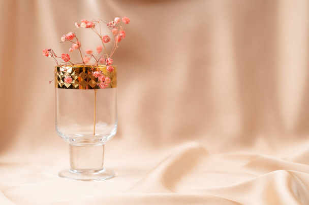 Beautiful glass goblet with golden rims and flowers inside on nude cream fabric - Photo, Image